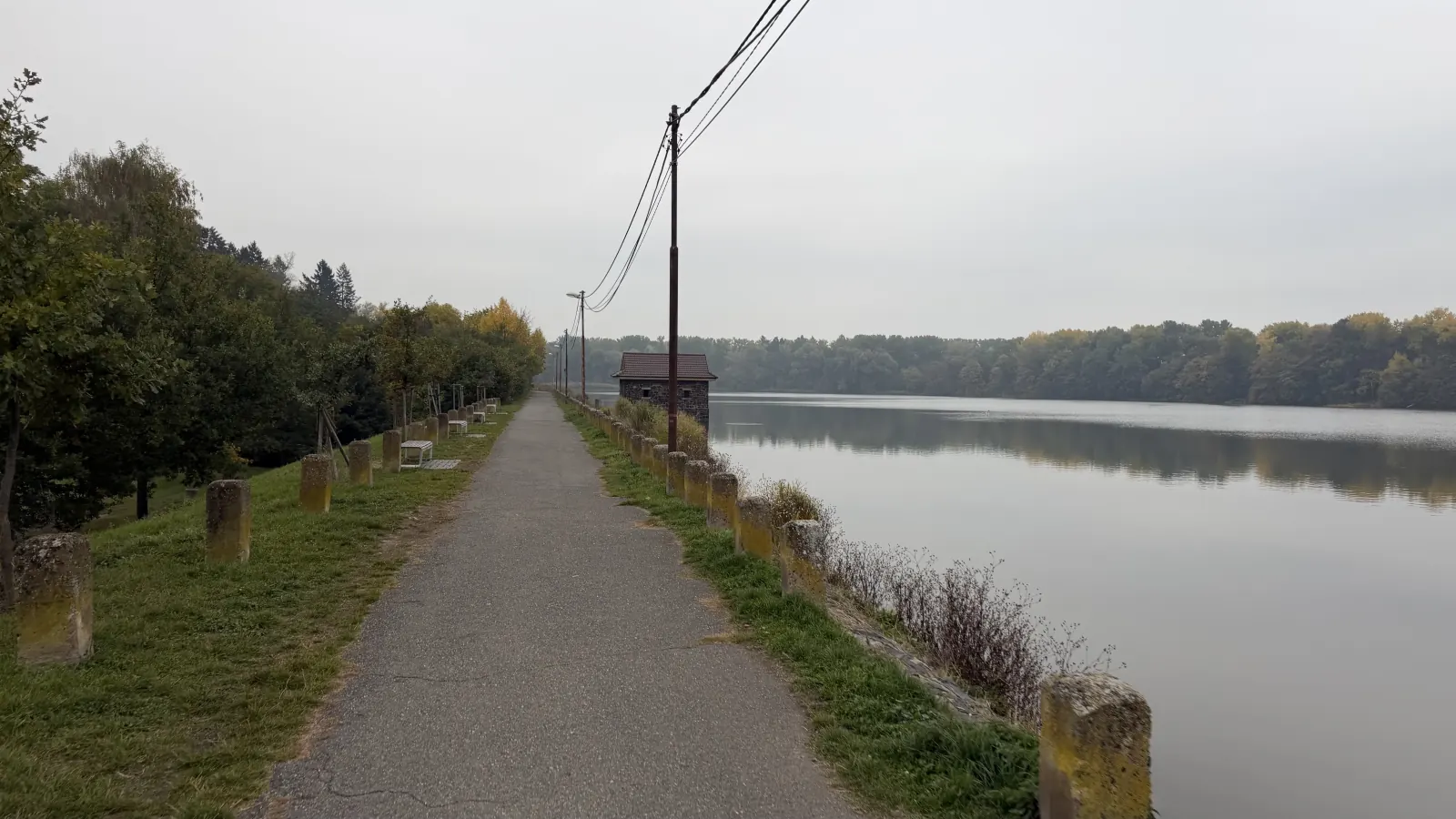 Cesta po hrázi rybníka, lavičky vlevo a klidná hladina vpravo