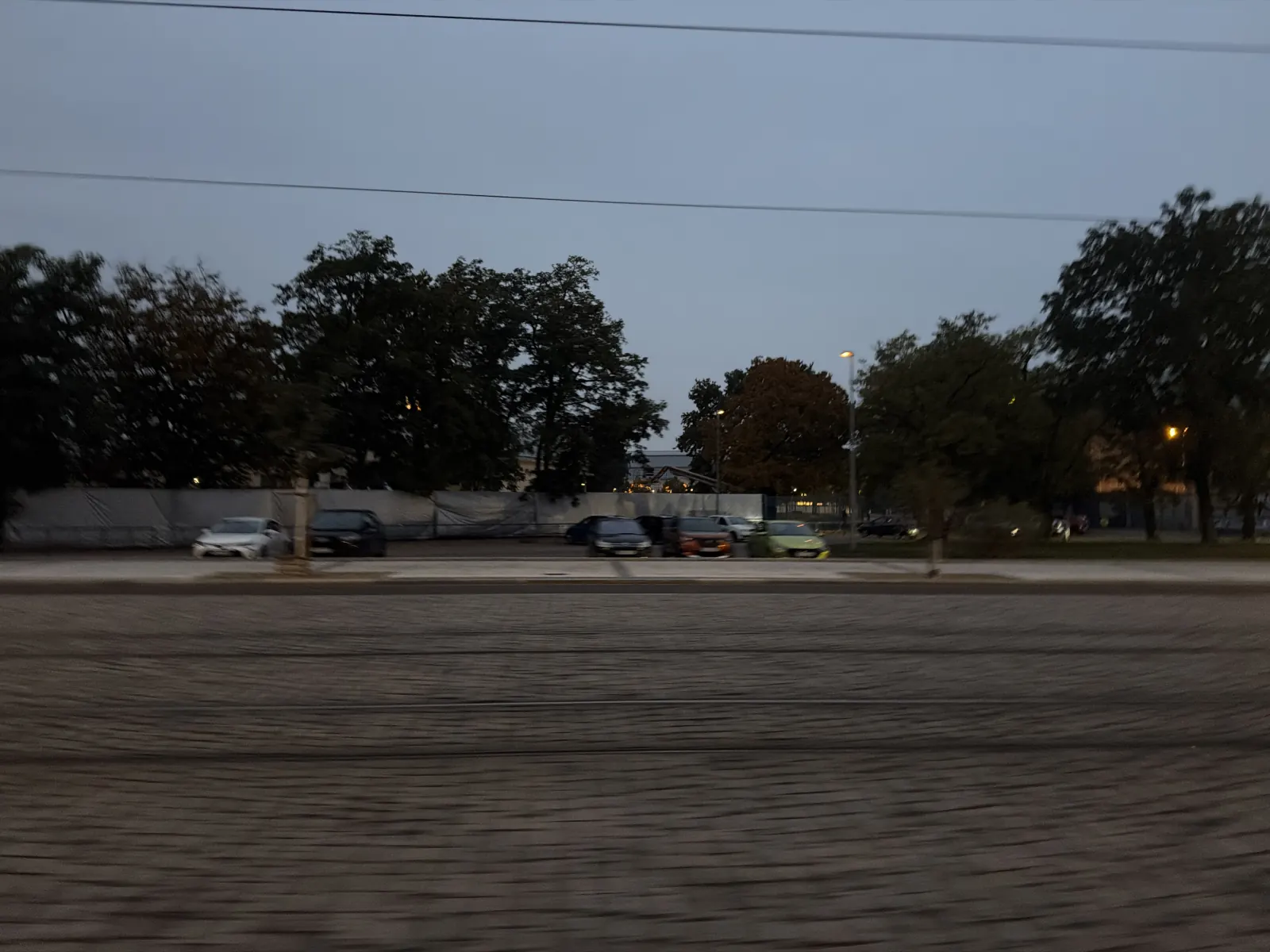 Večerní průjezd kolem tramvajových kolejí a zaparkovaných aut.