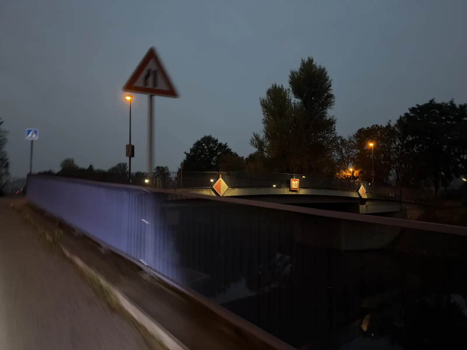 Most na ostrov před příjezdem k Trojské lávce, se zábradlím a rozsvícenými lampami.