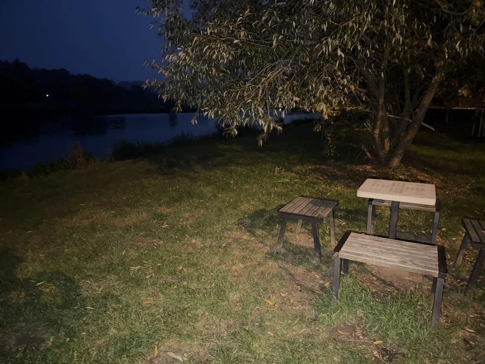 Posezení se stolkem a lavičkami pod stromem u noční řeky.