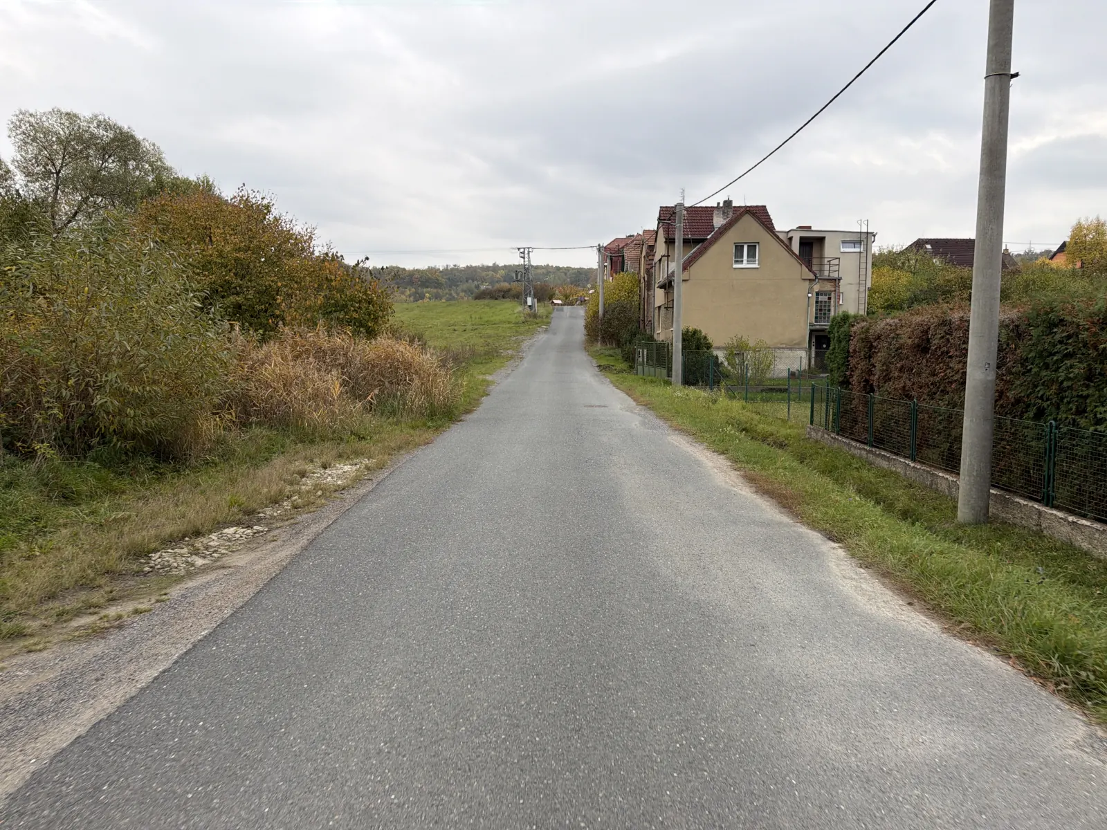 Silnice mezi domy a loukou pod zataženou podzimní oblohou