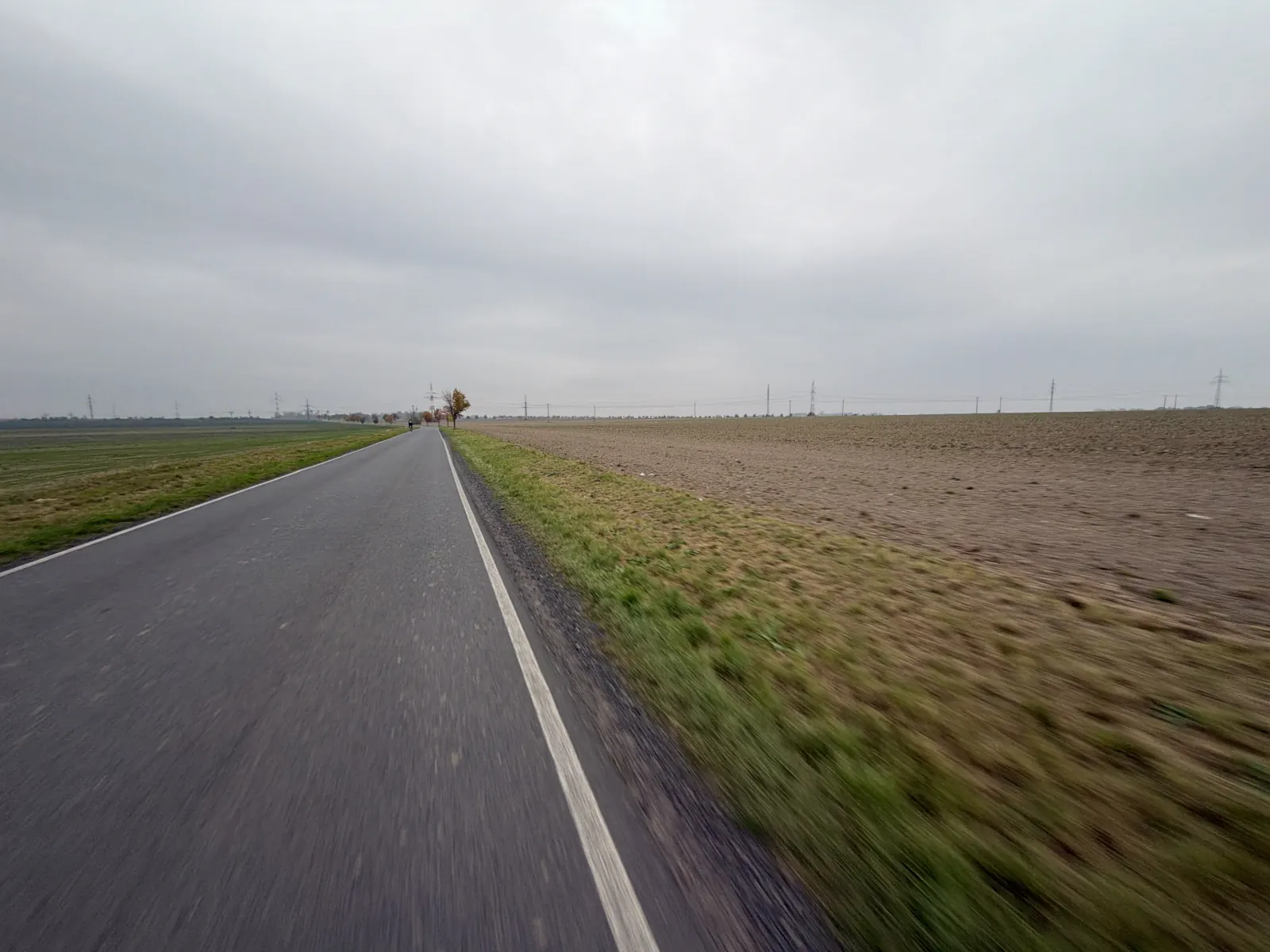 Rovná silnice mezi zeleným a zoraným polem pod zataženou oblohou