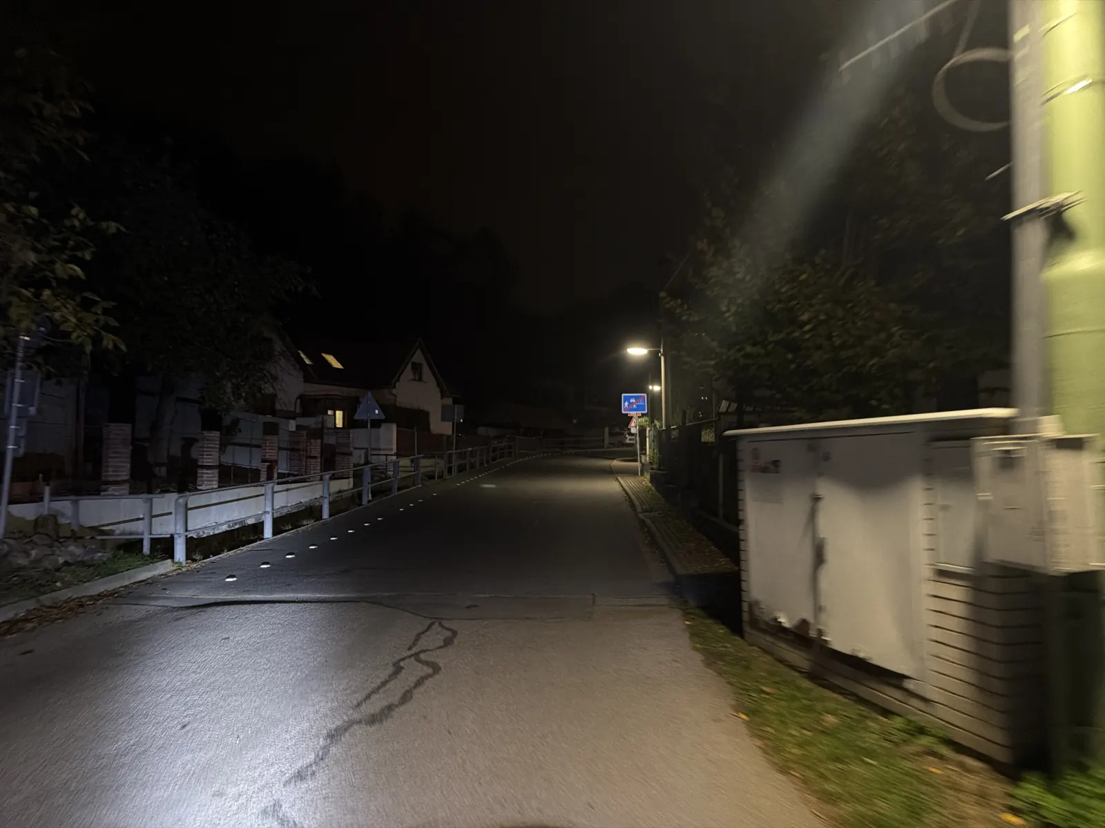 Osvětlená silnice mezi domy a stromy na začátku závěrečného výjezdu údolím.