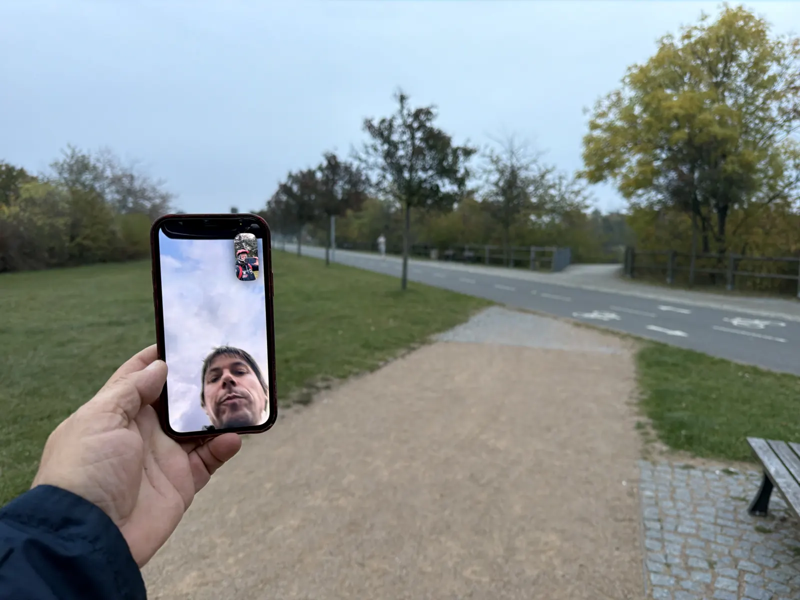 Telefon s videohovorem v ruce, v pozadí park a sportovní dráha